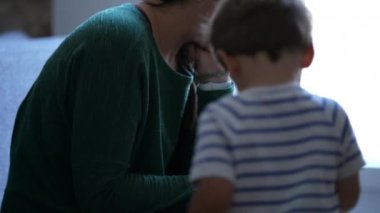 Child wanting mother attention who is looking at cellphone device. Little boy throwing himself on mother body feeling bored and hurt