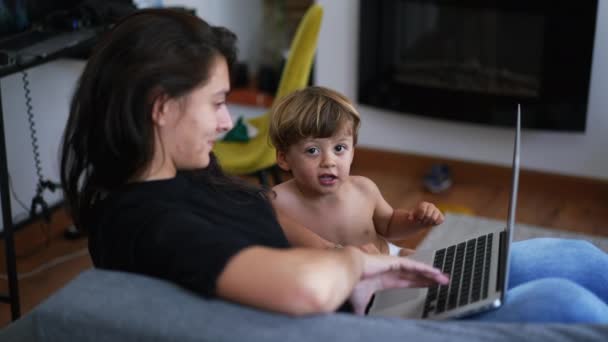 家庭から働くノートパソコンの画面の前で子供と母親の子育て 親座っています上のソファとともに幼児男の子見ますコンピュータ — ストック動画