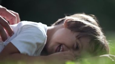 Neşeli çocuk mutlu yüz ifadesi güzel güneşli bir günde çimlerin üzerinde yatıyordu. Bir genç çocuk gülüyor ve gülümsüyor. Çocuk gıdıklanıyor.