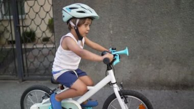 Şehir kaldırımında bisiklet süren küçük bir çocuk. Kask takan çocuk bisiklete biniyor. Çocuk hafta sonu aktivitesi