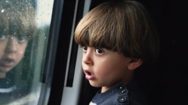 Küçük bir çocuk, hareket halindeki bir araçta pencerenin önünde trenle seyahat ediyor. Küçük çocuk tatilde gezer ve manzarayı seyreder.