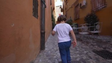 İtalyan caddesinde koşan küçük bir çocuğun arkasında. Tasasız çocuk, eski geleneksel Avrupa yolunu keşfediyor.