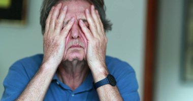 Older man covering face with hands, stressed and tired senior man in 70s feeling pressure