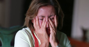Older woman feeling stress and pain, anxious person covering face with hands feeling anxiety