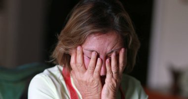 Older woman feeling stress and pain, anxious person covering face with hands feeling anxiety