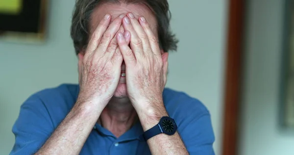 Older man covering face with hands, stressed and tired senior man in 70s feeling pressure