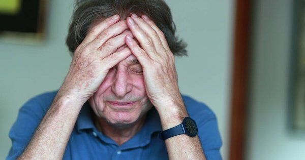 Older man covering face with hands, stressed and tired senior man in 70s feeling pressure