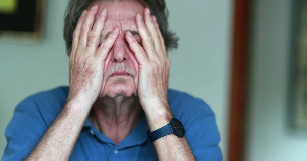 Older man covering face with hands, stressed and tired senior man in 70s feeling pressure