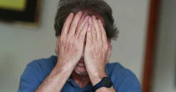 Stressed older man covering face with hands.Senior person feeling pain and stress