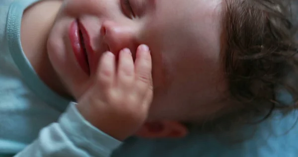 Tired baby rubbing eye and face with hands, sleepy child infant