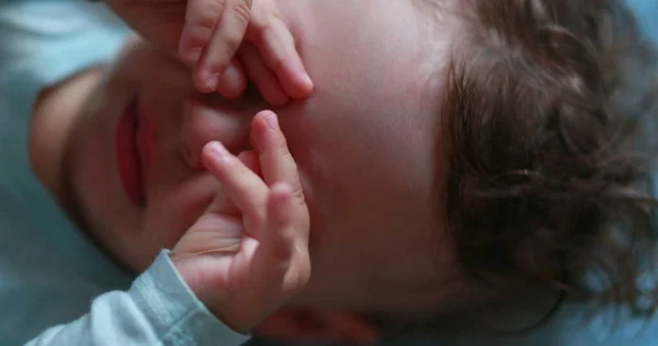 Tired baby rubbing eye and face with hands, sleepy child infant