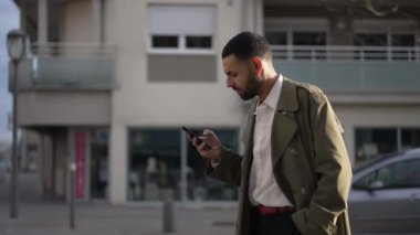 Sokakta ciddi bir ifadeyle yürürken telefonu tutan genç bir Arap. Ceket giyen bir Orta Doğulu mesaj okuyor.