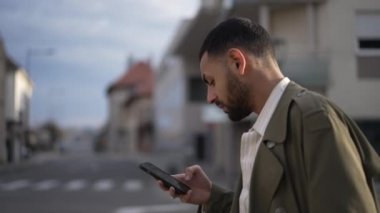 Orta Doğulu genç bir adam cep telefonu cihazına bakarak şehir caddesinde yürüyor. Kentsel çevrede içeriği kontrol eden bir Arap erkek. 