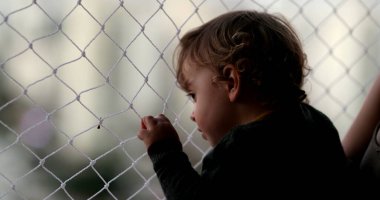 Baby looking outside pointing with finger, infant child holding net by window
