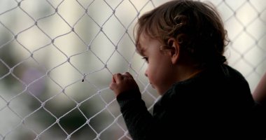 Baby looking outside pointing with finger, infant child holding net by window