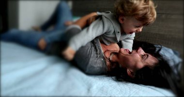 Mother and baby rolling together in bed, cute moment loving caring relationship between mom and child