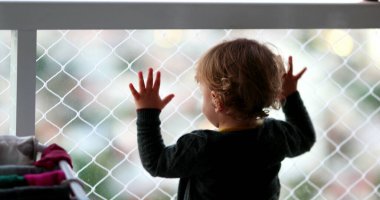 Toddler boy holding into balcony window wanting to go out