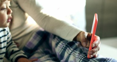 Mother and child talking to family member on cellphone in the morning bed