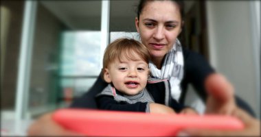 Toddler boy clapping hands while on mom lap watching smartphone screen