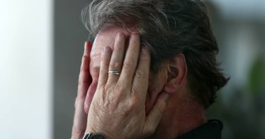 Older man rubbing eyes and face with hand, pensive and contemplative senior person