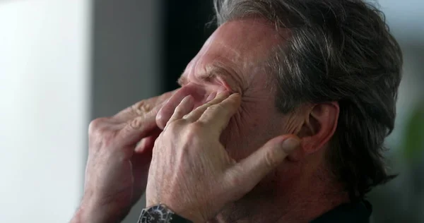 Older man rubbing eyes and face with hand, pensive and contemplative senior person