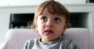 Toddler boy chewing food while watching media cartoon, infant child face staring