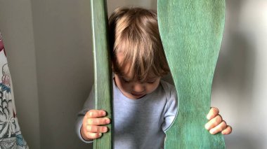 Bebek çocuk kameraya gülümseyen sandalyenin arkasına saklanır.