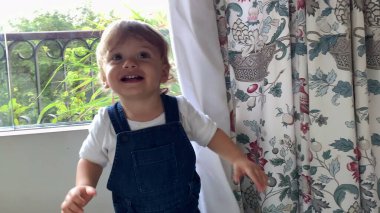 Heyecanlı mutlu bebek perdelerin arkasında el çırpıyor