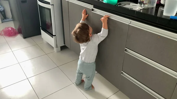 Baby toddler opening kitchen cabinets. infant on tippy toes reaching for objects