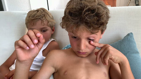 Два мальчика смотрят медиа-контент на планшете, сидя дома на диване