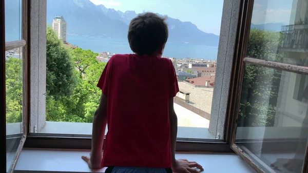 窓のそばに立って景色を楽しんでいる若い男の子 子供は美しい日を見て — ストック写真