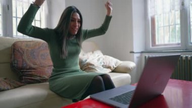 Mutlu genç bayan laptoptaki iyi habere muzaffer bir şekilde tepki veriyor. Orta Doğulu yetişkin kız evde başarıyı kutluyor