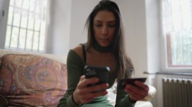 Ev koltuğunda oturan kişi internetten mal alıyor. Genç bir kadın internetten mal almak için kredi kartı bilgilerini kullanıyor. Çevrimiçi alışveriş kavramı