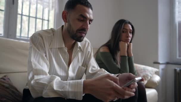 夫妇在危机中 男人在家里拿着手机时无视女朋友 女友想让网上社交媒体内容吸引伴侣的注意 坐在室内沙发上 — 图库视频影像