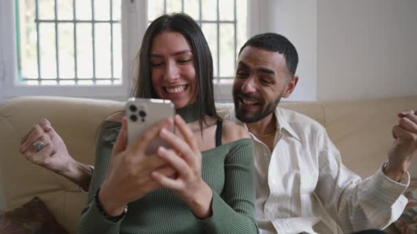 阿拉伯夫妇坐在家里 一边在智能手机上为好消息而欢欣鼓舞 快乐的女朋友和男朋友分享积极的信息 — 图库视频影像