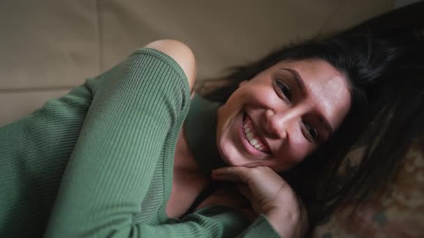 一个快乐的年轻女人躺在沙发上笑着 20多岁的成年女子感到幸福的脸 — 图库视频影像