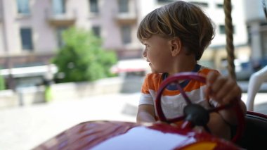 Güneşli bir günde atlı karıncada direksiyon tutan mutlu küçük bir çocuk. Oyuncak aracın içinde eğlenen çocuk