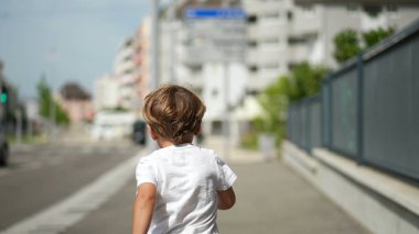Güneşli yaz gününde şehrin kaldırımında koşan mutlu aktif bir çocuk.