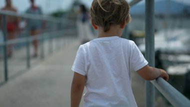 Güneşli bir günde küçük çocuğun sırtından. Sarışın bir erkek çocuk, güzel bir yaz gününde düşünceli bir şekilde dışarı çıkar.