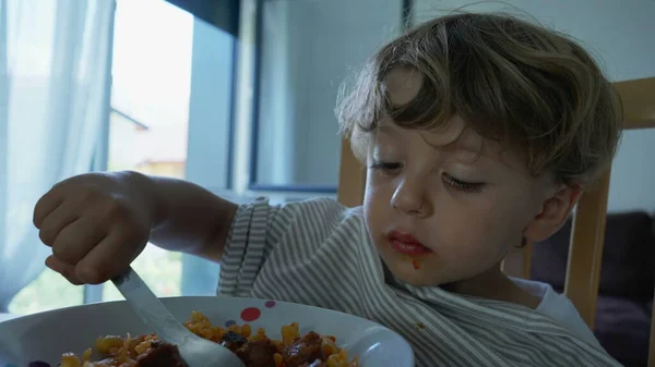 stock image Child eating pasta food for lunch at home. Authentic lifestyle scene of kid eats noodles by himself with fork