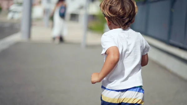 stock image One joyful small boy running outdoors in city street sidewalk. Back of child runner in urban environment