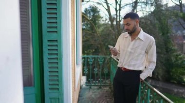 Ortadoğulu bir adam balkonda telefonu kontrol ediyor. Modern teknolojiyi kullanan Faslı bir Arap, internette geziniyor.