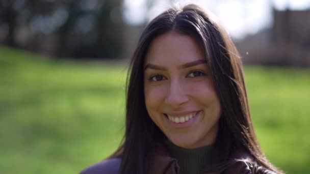 一个快乐的年轻女子站在公园外对着摄像机微笑的画像 20多岁的一个对自然表情感到满意的成年女孩的合影脸 — 图库视频影像