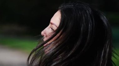 Mutlu, kendine güvenen genç bir kadın parkta yürüyor başını yana çevirip gülümsüyor.