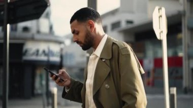 Şehirde elinde telefonla dolaşan bir Arap 'ın profili. Şehirdeki akıllı telefondan internete giren Orta Doğulu bir erkeğin görüntüsü.