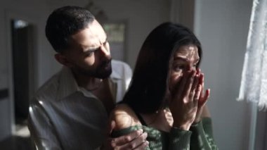 Bir Arap erkek arkadaşı, perdelerden süzülen güneş ışığıyla pencerenin kenarında duran kederli kız arkadaşını teselli ediyor. Zor zamanlarda empatik ve destekleyici çift