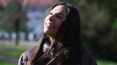 Düşünceli, mutlu genç bir kadın parkta güneş ışığı ve temiz hava alarak yürüyor. Barışçıl meditasyoncu yetişkin kız 20 'li yaşlarda gülümsüyor.