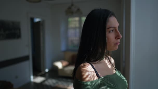 一人の瞑想的な若い女性が窓の外を見て立っている 20代の思慮深い女性は家の中に立つ — ストック動画