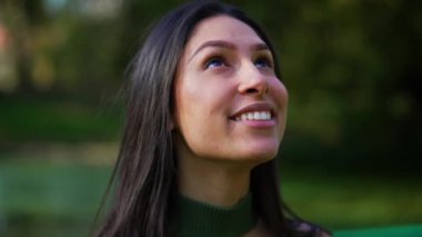 Sadık bir ifadeyle gökyüzüne bakarken gülümseyen umut dolu genç bir kadın.