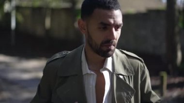 Genç, modaya uygun bir Arap adam dışarıda duruyor ve ceketini düzeltiyor.